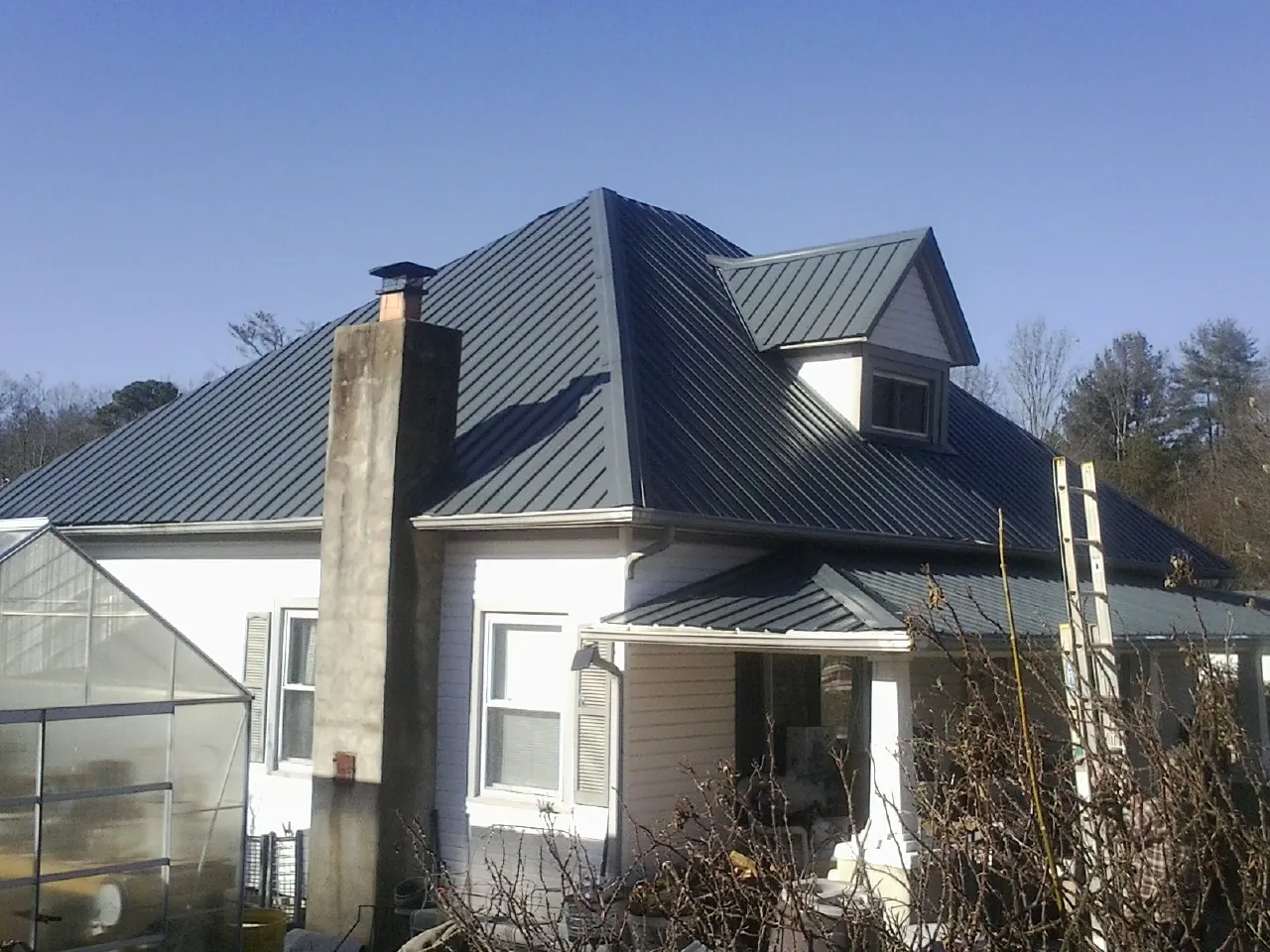Dark blue standing seam metal roof on a white farmhouse with dormer — Slate & Tile Roof Repair by Roofing Brothers in Beaufort