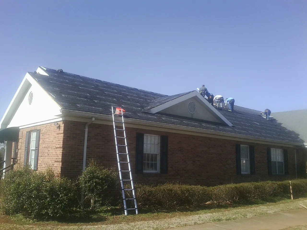 Crew tearing shingles off a brick ranch roof with a ladder set — Metal Roof Repair work by our crew in Beaufort