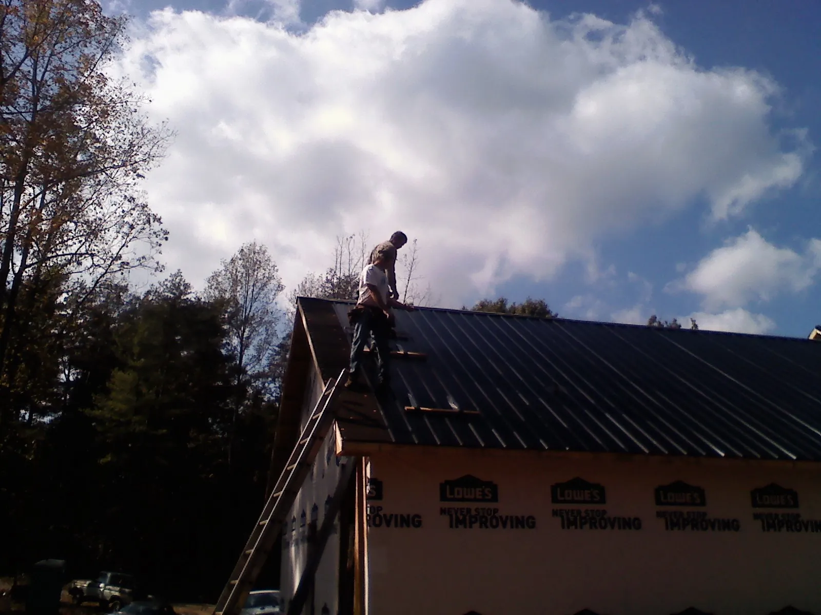 Roofer fastening dark metal panels high against a cloudy sky, from a Roof Inspection job in Beaufort