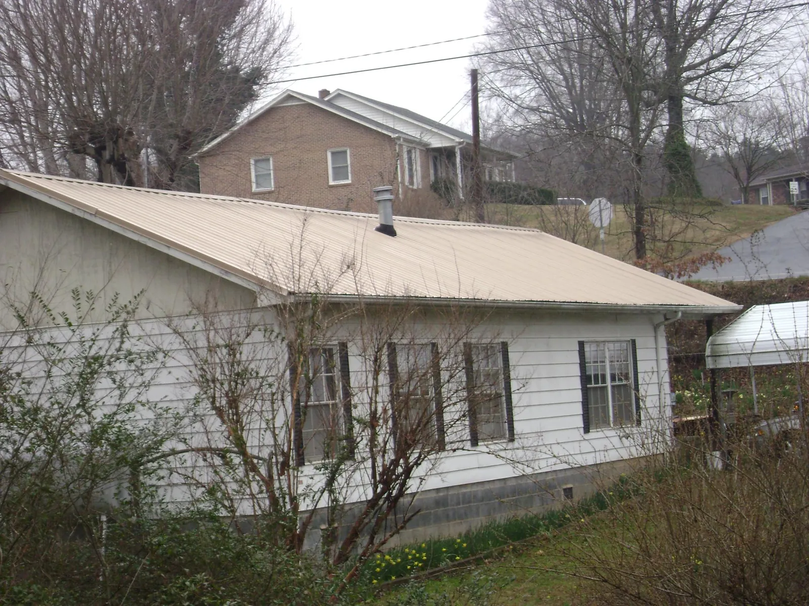 Tan metal roof on a white sided house set into a hillside — Commercial Roofing by Roofing Brothers in Beaufort